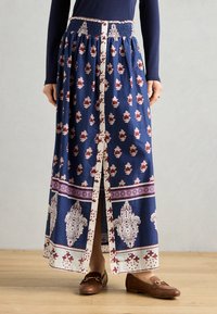 Longue jupe marine ornée d'imprimés floraux et paisley, d'une taille smockée, de détails de boutons sur le devant et de bandes d'accent blanc et bourgogne contrastantes.