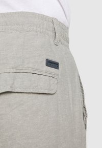 Light gray linen shorts with a back pocket. Features a dark blue label with "Lindbergh" branding. Textured fabric, casual design.