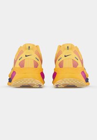 Αθλητικά παπούτσια Nike για τρέξιμο με κίτρινο επάνω μέρος, μοβ λεπτομέρειες, ριγέ σχέδια και ανάγλυφη εξωτερική σόλα για πρόσφυση. Πλάγια όψη που δείχνει τις λεπτομέρειες του σχεδιασμού.