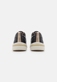 Sneakers neri con tomaia in pelle texturizzata, dettagli beige sul tallone e suola in gomma bianca. Design minimalista; punta tonda.