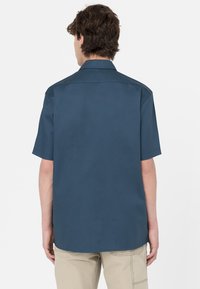 Camicia a maniche corte di colore blu scuro, realizzata in tessuto morbido, con colletto classico e orlo dritto, priva di motivi o decorazioni visibili.