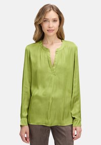 Blusa verde a maniche lunghe in tessuto lucido con scollatura a V e dettagli con arricciatura alla scollatura, con vestibilità ampia e accenti plissettati.