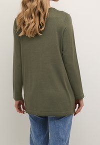 Olivově zelený svetr s dlouhým rukávem a kulatým výstřihem, vyrobený z měkké látky, s volným střihem, bočními rozparky a žebrovanými manžetami.