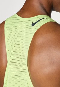 Limonasto zelena brezrokavna športna majica z mrežasto teksturo, ki ima črno Nike logotip na rami, zasnovana za zračnost in gibljivost.
