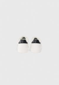 Zapatillas bajas blancas de cuero liso, con un acento en el talón negro en contraste, detalles cosidos y forro interior texturizado.