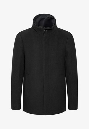 Sort yderjakke med seks knapper, marineblå sweater under, blå denim jeans og beige/hvide sneakers med sorte accenter.