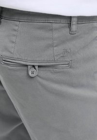 Pantalones grises con tejido texturizado, que presentan un pequeño bolsillo trasero asegurado por un botón y un sutil logo grabado encima del bolsillo.