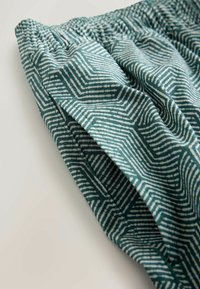 Zeleno-biely vzorovaný textil s geometrickými cikcak líniami, vybavený elastickým pásom a bočným vreckom.