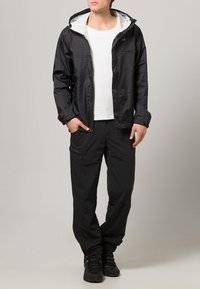 Chaqueta impermeable negra con un forro interior blanco en contraste, combinada con pantalones negros a juego. El atuendo presenta un dise�ño sencillo y práctico.