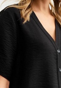 Černá košile s knoflíky a texturovanou tkaninou, s výstřihem do V a krátkými rukávy, se třemi knoflíky vpředu.