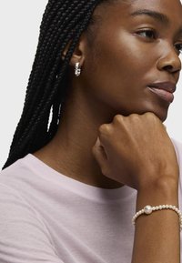 Pendientes de plata con un diseño floral, usados con una camiseta rosa clara. Pulsera de perlas con una perla redonda y un acento de diamante.