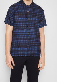 Korteblauwe button-up shirt met korte mouwen en een ruitenpatroon, met horizontale en verticale lijnen in verschillende tinten blauw.