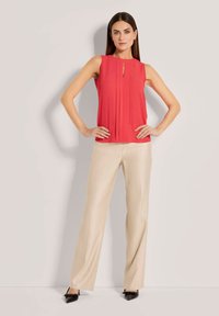 Rode mouwloze blouse met plooien en een keyhole halssnit, gecombineerd met crèmekleurige wijde broek. De broek heeft een gladde textuur en een subtiele glans.
