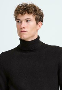 Črna pulover z visokim ovratnikom iz mehkega pletenega materiala, ki ima rebrast ovratnik in sproščen kroj. Tekstura se zdi gladka in topla.
