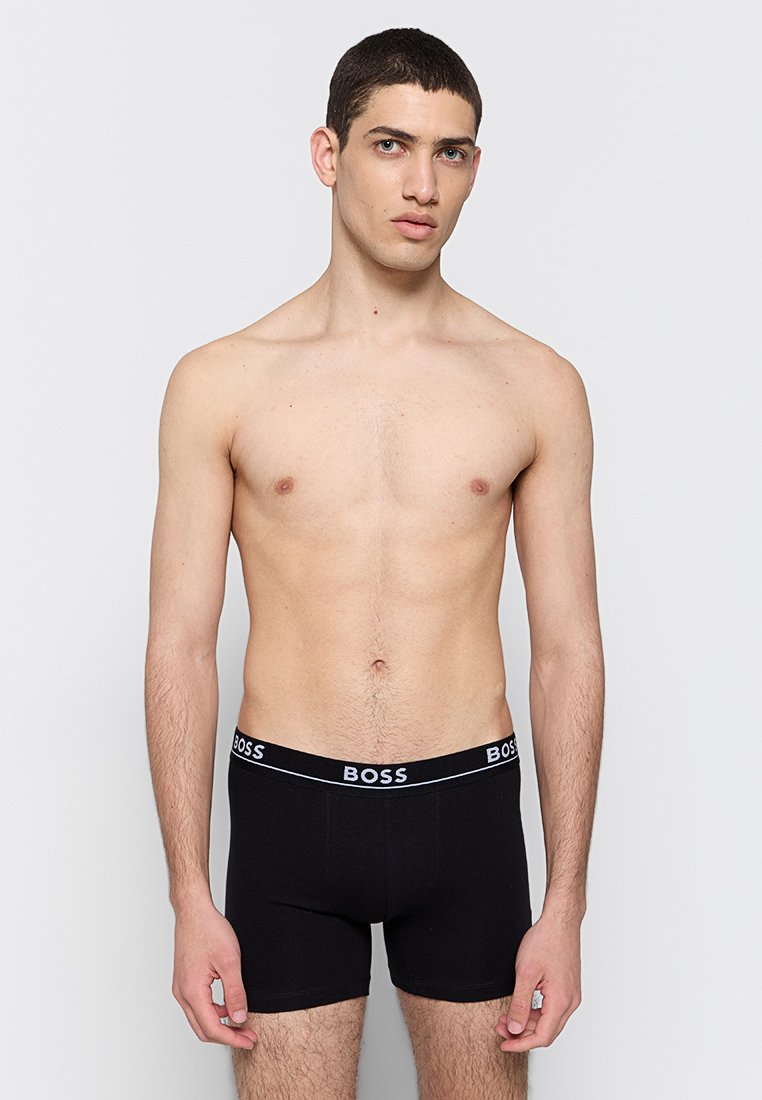 Boxers noirs en coton avec une texture lisse, dotés d'une ceinture élastique marquée en blanc, modèle présentant une vue de face.