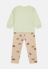 Kaksiosainen lasten asu, joka koostuu vaaleanvihreästä collegepaidasta ja beigeistä legginsseistä, joissa on toistuva kuvitus sarjakuvakarhuista. Pehmeä puuvillakangas.