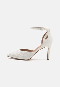 Scarpa con tacco alto bianca, punta affusolata, cinturino alla caviglia e dettagli in pizzo sulla tomaia; presenta un retro in pelle liscia e un tacco a stiletto.