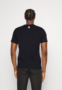 Svart kortärmad t-shirt, tillverkad av bomull, med rundad halsringning och en liten vit logotyp på den övre ryggen. Slät textur.