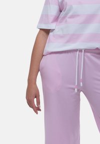 Helles, rosa Baumwoll-T-Shirt mit weißen horizontalen Streifen; kombiniert mit hellrosa Hosen, die einen Kordelzugbund mit weißen und rosa Akzenten haben.