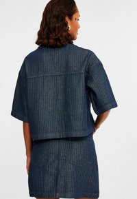 Blauwe denim cropped jas met een gestreept patroon en korte mouwen, gecombineerd met een bijpassende rok met achterzakken en een aansluitende pasvorm.