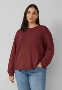 Bordeaux oversized sweatshirt met een ronde hals en lange mouwen, gemaakt van een zachte stof, gecombineerd met lichtblauwe jeans.