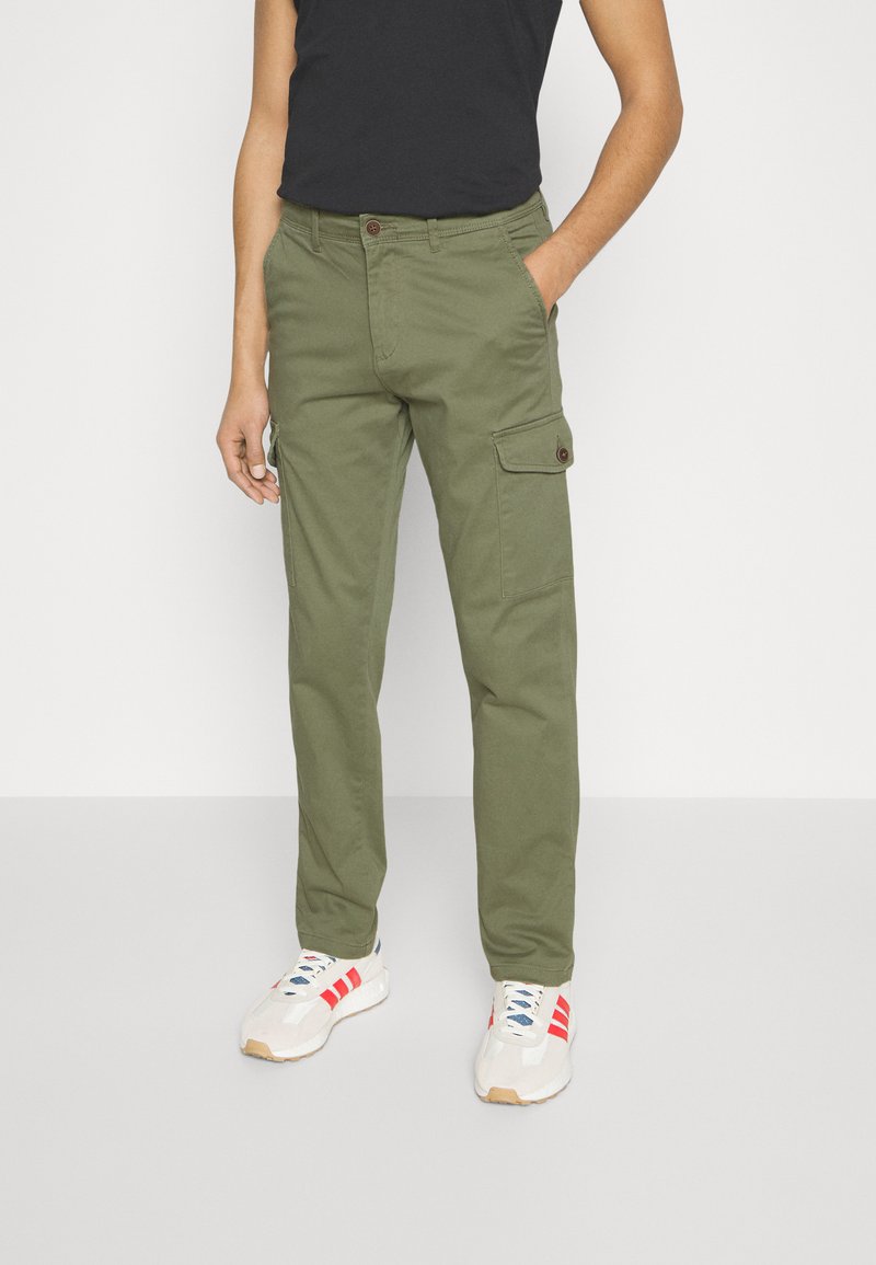 Olive cargo pants with side pockets, a button closure, and belt loops, paired with white sneakers featuring red accents.