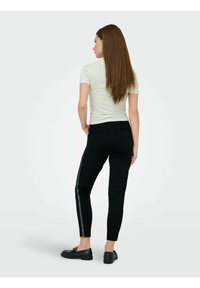 Svarte, innsnevrede bukser med en blank sidekant stripe, kombinert med en lyse farget, tettsittende topp. Jevnt stoff med et avslappet, strømlinjeformet design.