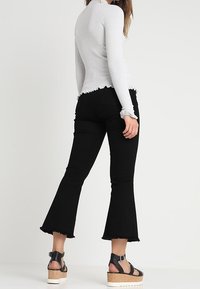 Harmaa ribbineulottu pitkähihainen paita, jossa on aaltoileva helma. Yhdistetty mustiin liehukkeellisiin farkkuihin, joissa on viimeistelemättömät reunat, ja mustiin korokepohjaisiin sandaaleihin.