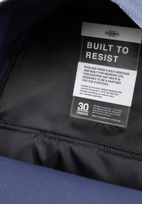 Intérieur du sac Eastpak Day Pak'r, avec une doublure en tissu noir, une étiquette d'entretien portant le texte "CONÇU POUR RÉSISTER", et un extérieur bleu lisse.