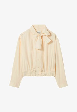 Blusa de color durazno claro con un lazo en el cuello, mangas largas, frente abotonado y dobladillo con elástico recogido. Tela suave y lisa, diseño minimalista.