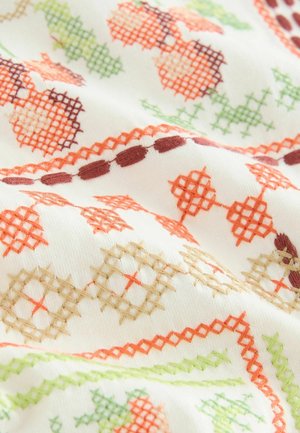 Weißer Stoff mit aufwendiger Stickerei in Orange, Grün und Braun, der geometrische Muster und Kreuzstichdetails aufweist.