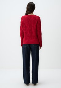 Maglione rosso lavorato a maglia con un motivo testurizzato, dotato di collo rotondo e maniche lunghe, abbinato a jeans in denim scuro a gamba dritta.
