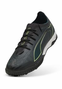 Svart atletisk sko med en texturerad ovandel, kontrasterande limegröna detaljer, sex ögla och en vit dämpad sula.