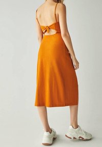 Orange midi klänning med spaghettiband, detalj med knytning bak, texturerat tyg och utskärning. Matchad med vita sneakers.