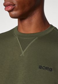 Sudadera verde oliva con cuello redondo, con un detalle de costura diagonal en el cuello y "BORG" bordado en negro en el pecho.