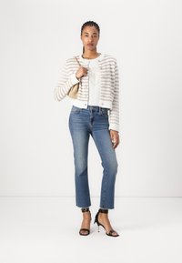Gestreifter Cardigan in Creme und Beige, kurze Länge; weißes Oberteil mit geprägtem Design; hellblaue Jeans mit mittlerem Bund, knöchellang; schwarze Sandalen mit Absatz.