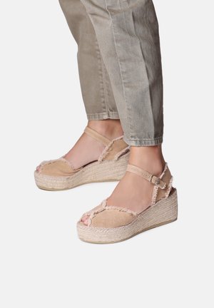 Beige espadrille wedge sandals featuring a textured fabric upper, open toes, and adjustable ankle strap with a buckle. Jute-wrapped sole.