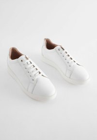Baskets en cuir blanc avec des bouts ronds, des cols rembourrés et six œillets. Texture lisse avec un design minimaliste et des semelles en caoutchouc crème.
