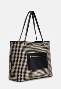 Sac cabas tissé noir et beige avec de longues poignées noires et une poche zippée noire à l'avant avec des détails de fermeture éclair dorés.