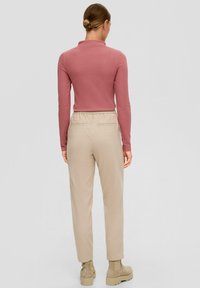 Pitkähiha, istuva paita pölyruusun värissä, yhdistettynä vaaleanbeigeihin korkeavyötäröisiin housuihin, joissa on joustava vyötärö ja sivutaskut.