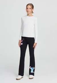 Pantaloni neri con stampe di cartoni animati rosa e blu, abbinati a una maglietta bianca a maniche lunghe. Il tessuto è morbido e la vestibilità è comoda.