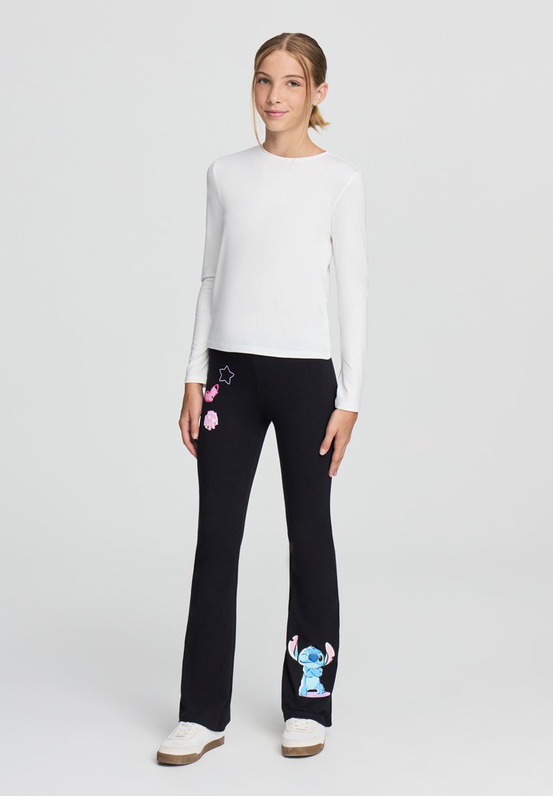 Pantaloni neri con stampe di cartoni animati rosa e blu, abbinati a una maglietta bianca a maniche lunghe. Il tessuto è morbido e la vestibilità è comoda.