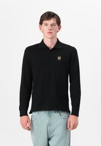 Pikemate musta polo-särgid, pikad varrukad ja krae, vasakul rinnal kuldne embleem. Valmistatud siledast kangast; lõdva istuvusega ning ribadega mansettidega.