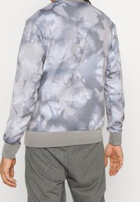 Sudadera gris con estampado de tie-dye y un acabado texturizado, cuello redondo, puños y dobladillo de canalé. Combinada con pantalones de chándal grises.