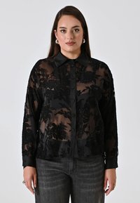 Black sheer blouse with floral embroidery, long sleeves, button front, and classic collar. Textured fabric contrasts with solid cuffs.