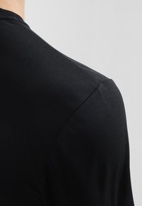 Camisa negra de manga corta con un tejido texturizado, que presenta un cuello redondo clásico y un diseño ajustado en los hombros.