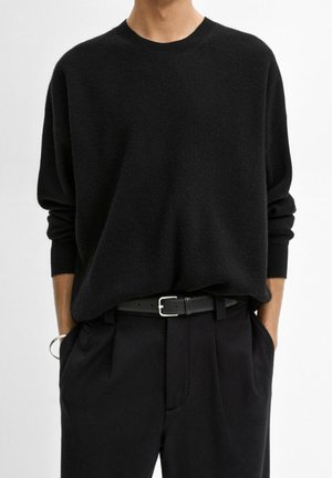 Czarny sweter prążkowany o luźnym kroju, okrągłym dekolcie i opadających rękawach; połączony z czarnymi spodniami o klasycznym kroju i czarnym paskiem.