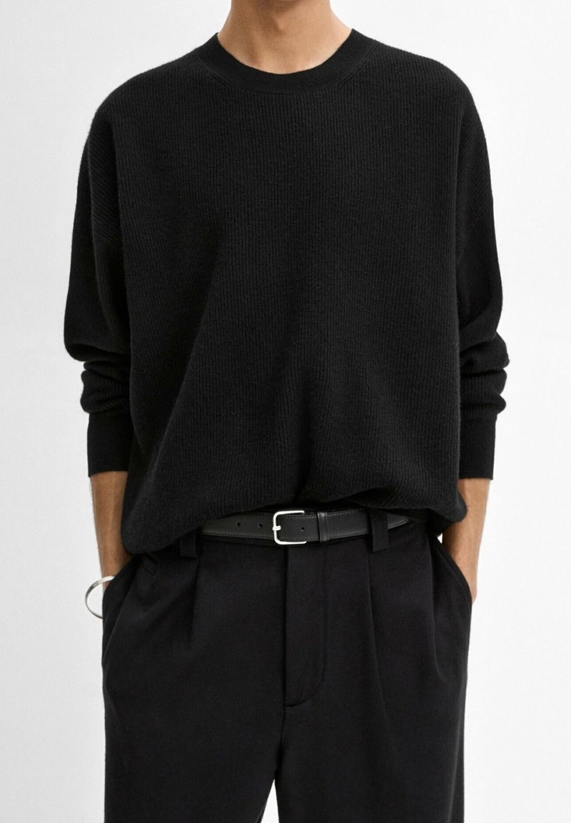 Czarny sweter prążkowany o luźnym kroju, okrągłym dekolcie i opadających rękawach; połączony z czarnymi spodniami o klasycznym kroju i czarnym paskiem.