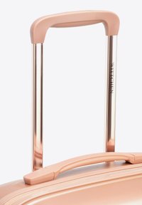 Roze harde koffer met een textuurafwerking, voorzien van een uittrekbare metalen handgreep en een handgreep aan de bovenkant; merk zichtbaar op de handgreep.