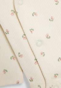 Beige csíkozott bodysuit kis rózsaszín rügymintával és zöld levelekkel; patent gombokkal és puha, texturált anyaggal rendelkezik.